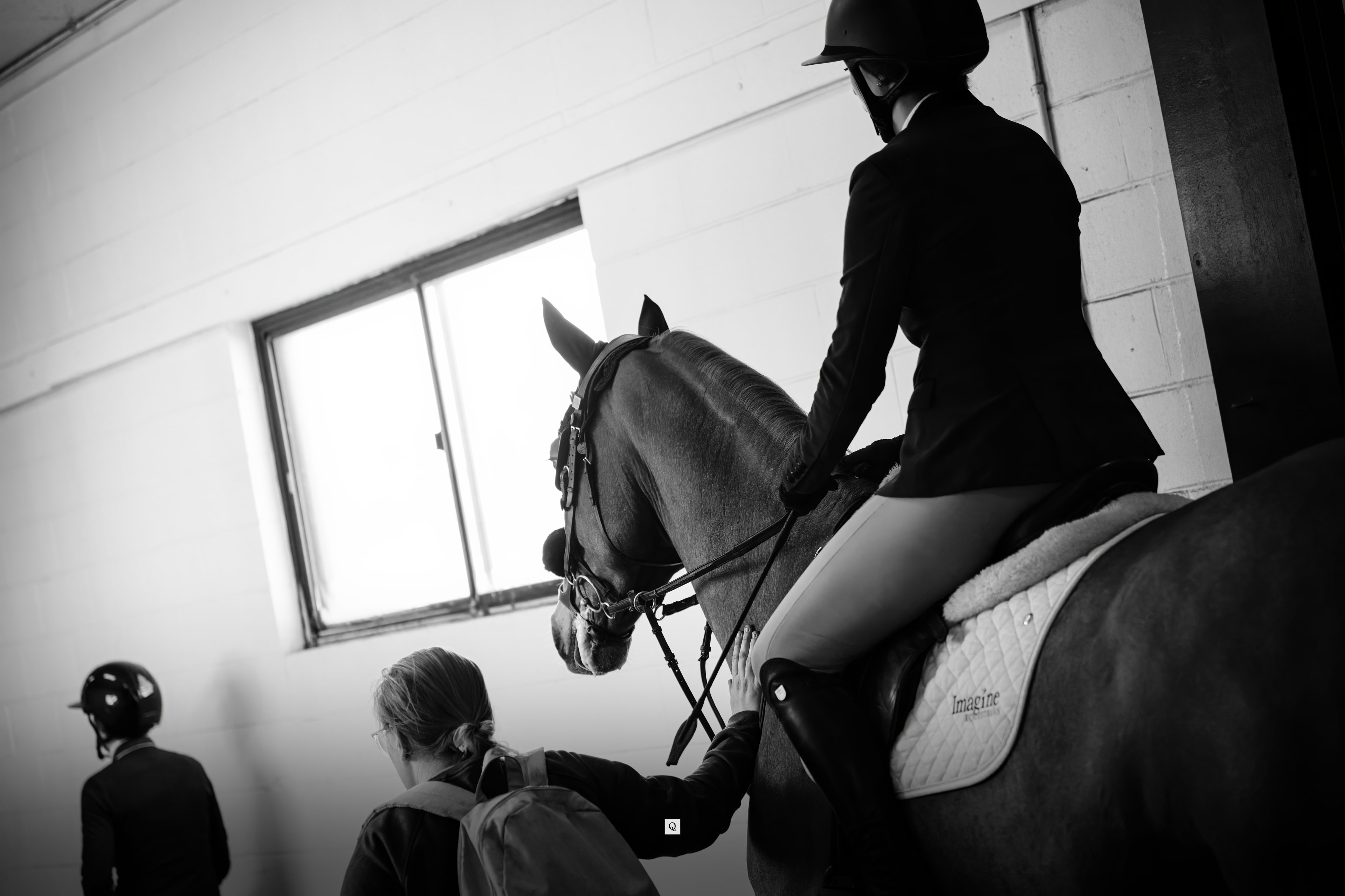 A groom attends to a rider and horse in an indoor arena before competition